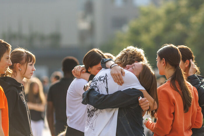 Group of young people comforting each other outdoors after Austrian shooter incident, reflecting on chilling video and rescue delay.