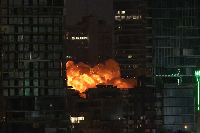 Large explosion with bright flames and smoke in a city skyline at night, related to Trump approving Iran attack plan tension.