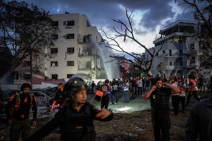Rescue teams and crowds calm on rooftops amid blazing rockets tearing toward Israel at a damaged building site.
