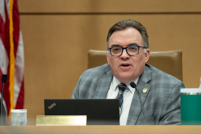 Politician speaking at a hearing, discussing the alleged shooter in lawmakers attack who fled into woods and now in custody.