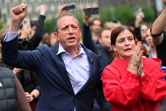 Brad Lander raising fist and supporting immigrant rights at public rally with crowd and cameras in background