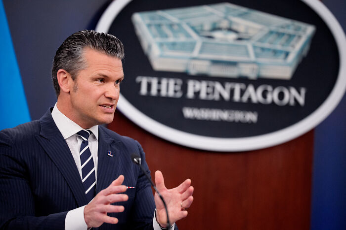 Pentagon spokesperson in suit speaking at press briefing on U.S. stance amid Iran nuclear retaliation threats.