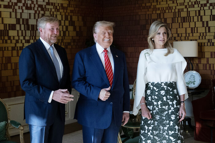 Donald Trump smiling between Dutch Queen and King in formal setting, highlighting facial expressions during public appearance.