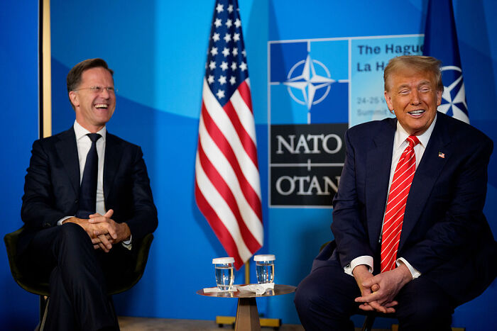 Donald Trump and NATO leader Mark Rutte sitting together with flags in the background during a NATO event.