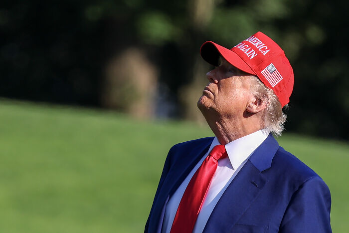 Donald Trump outdoors in a blue suit and red hat, symbolizing the dynamic Elon Musk and Donald Trump rivalry.