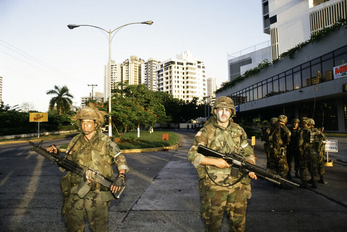 Two soldiers in combat gear stand guard on an urban street, highlighting ICE forces purple heart veteran self-deport issue.