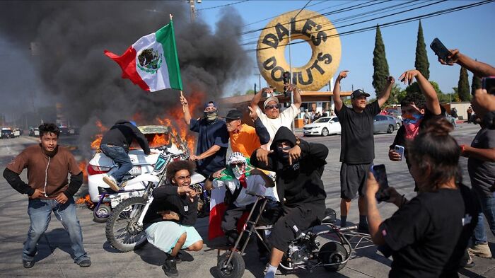 Protesters gather near burning car with Mexican flag during LA riots as heavily armed cops enforce law and order.
