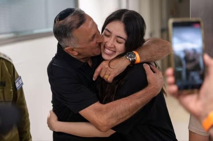 A relieved October 7 hostage warmly hugging a man while being photographed in an indoor setting.