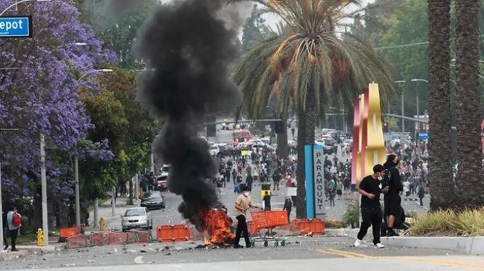 Crowd near burning fire and thick black smoke on street during LA riots with California Governor Gavin Newsom related tensions.