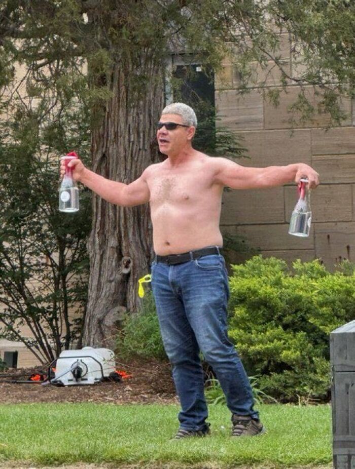 Shirtless man wearing sunglasses holding two bottles, linked to FBI identifying suspect in flamethrower attack in Colorado protest.