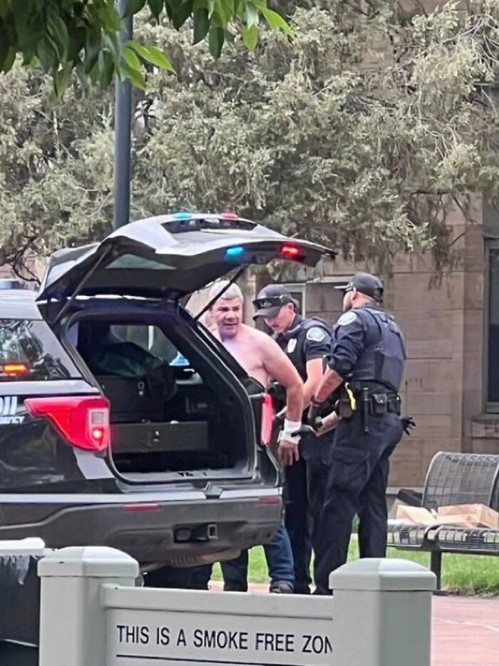 Man being detained by police near police vehicle during FBI suspect arrest in Colorado protest flamethrower attack case