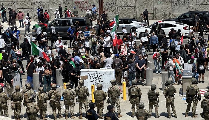 Crowd protests amid LA riots with police and military presence, linked to Donald Trump comments on Gavin Newsom arrest.