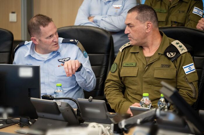 Two military officers in uniform discussing Iran firing 100 drones at Israel amid Revolutionary Guard Corps strike.