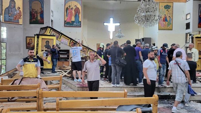 People gathered inside damaged Greek Orthodox church after suicide bombing in Syria with visible debris and broken furniture.