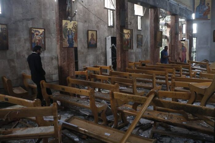 Damaged interior of Greek Orthodox church in Syria after suicide bombing, with scattered debris and broken pews.