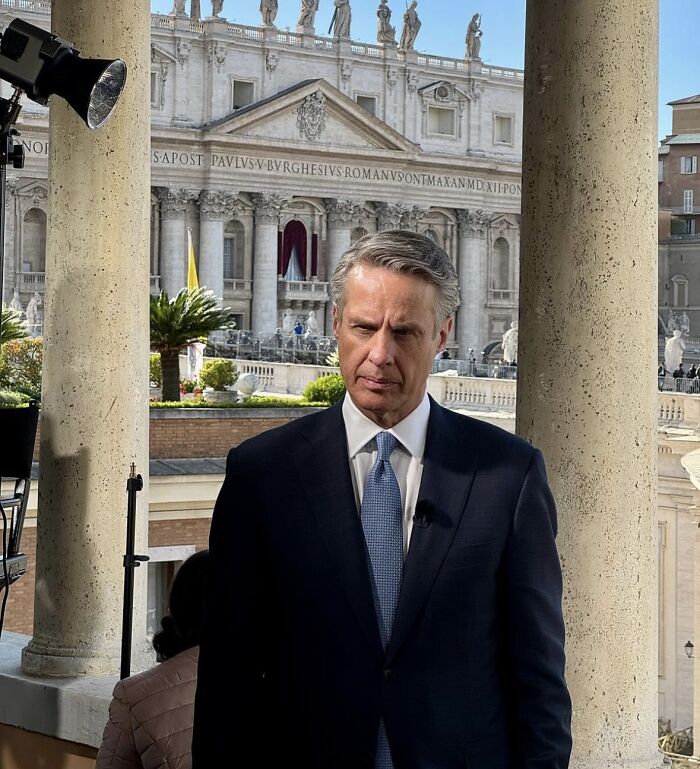 Journalist in a dark suit reporting outdoors near historic columns, linked to ABC News axe after Trump and Stephen Miller commentary.