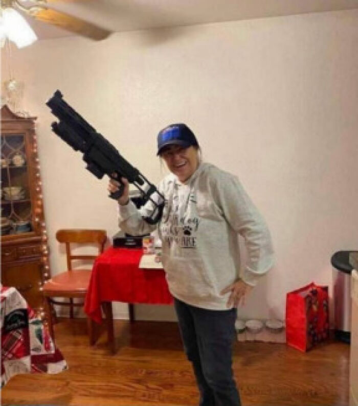 Woman wearing a cap indoors holding a large black toy gun, representing Jan 6 rioter and MAGA Granny incident.