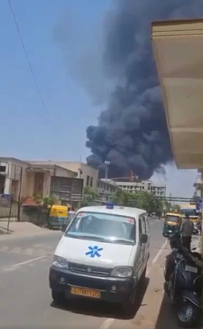 Emergency ambulance on street with thick black smoke in the sky from Air India flight crash near city buildings.