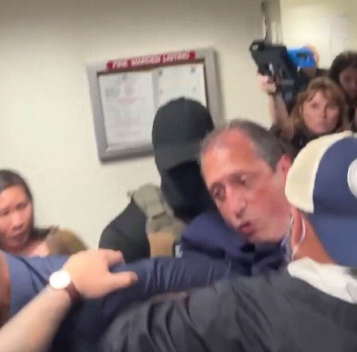 Brad Lander being detained by ICE officers in a crowded room while stepping in to help an immigrant in New York.