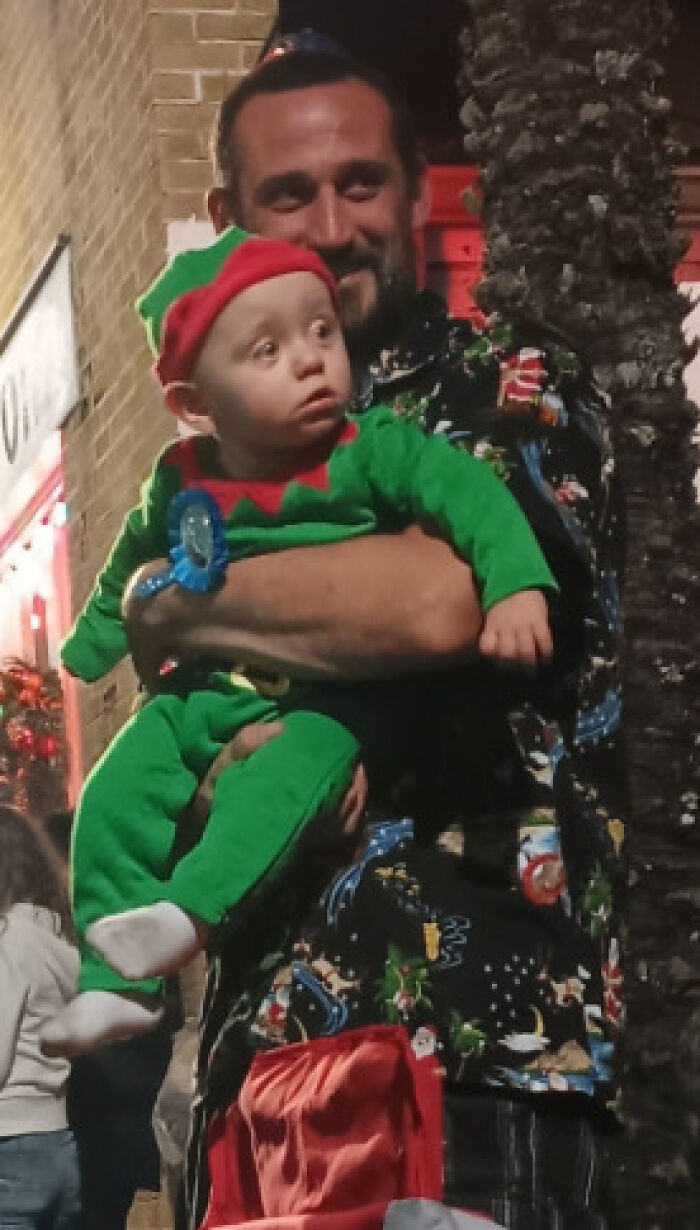 Man holding baby boy dressed in green elf outfit, related to baby boy dies in boiling car Florida news story.