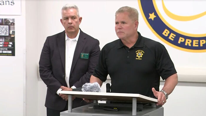 Two firefighters killed and one injured after sniper lures them into Idaho wildfire trap, officials speaking at podium.