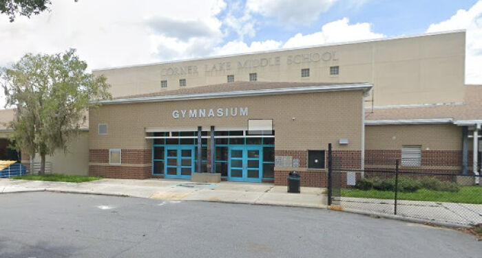 Corner Lake Middle School gymnasium entrance with blue doors and surrounding parking area under a partly cloudy sky.