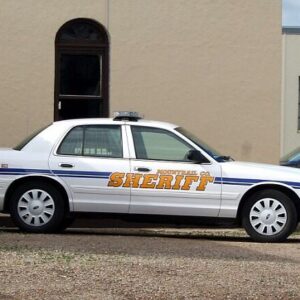 White sheriff patrol car parked outside a beige building related to foster parents charged with killing 3-year-old girl