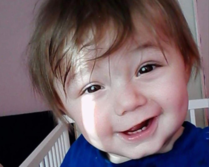 Toddler with a joyful expression in a blue shirt, highlighting abuse and painfully thin condition concerns.