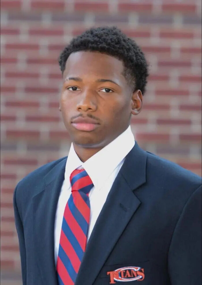 Karmelo Anthony, 17, wearing a school blazer and striped tie, posing in front of a brick wall background.
