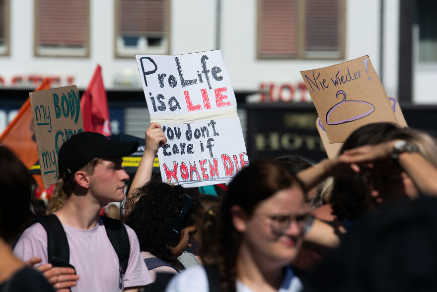 Protesters holding signs against abortion laws, highlighting issues related to brain-dead pregnant woman in Georgia case.