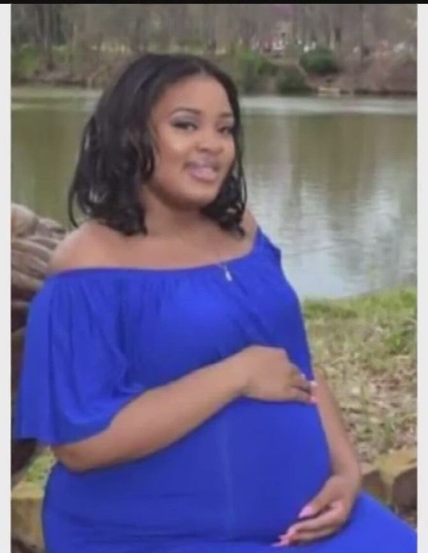 Pregnant woman in a blue dress sitting outdoors by a lake, relating to brain-dead pregnant woman kept alive Georgia abortion ban.
