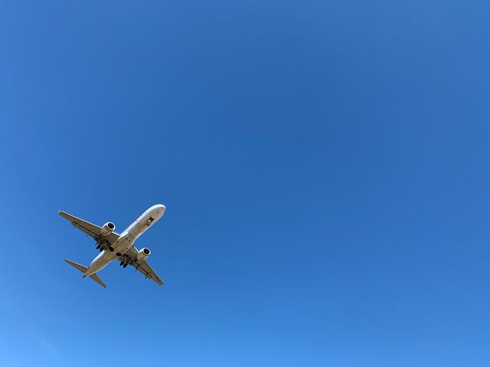 Commercial airplane flying against a clear blue sky representing Trump travel ban limiting entry from 19 countries to the US