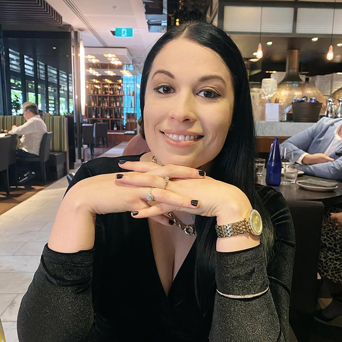 Woman sitting in a restaurant with hands clasped, representing Aussie mom accused of murdering daughter in hospital news.