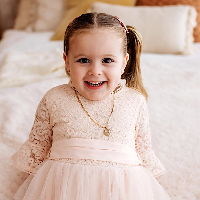 Smiling young girl in a lace dress wearing a gold heart necklace, related to Aussie mom accused of murdering daughter news.