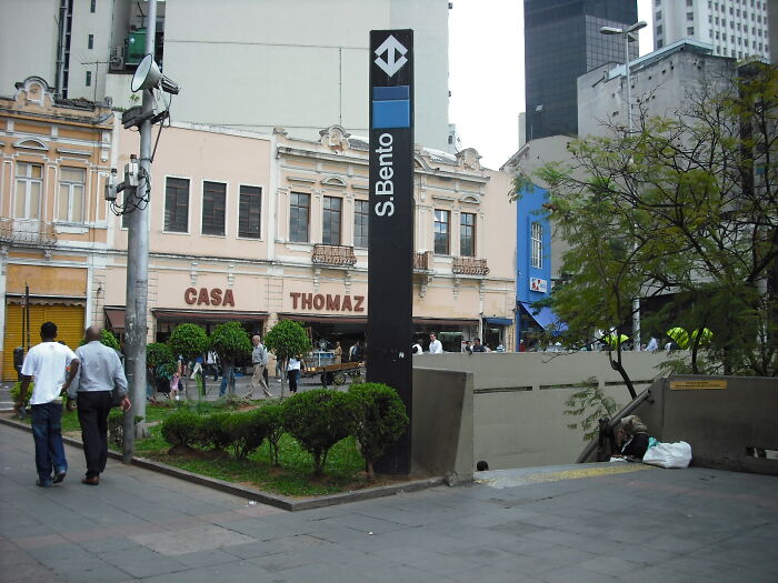 Subway station entrance with commuters walking near S Bento sign and historic building in the background.