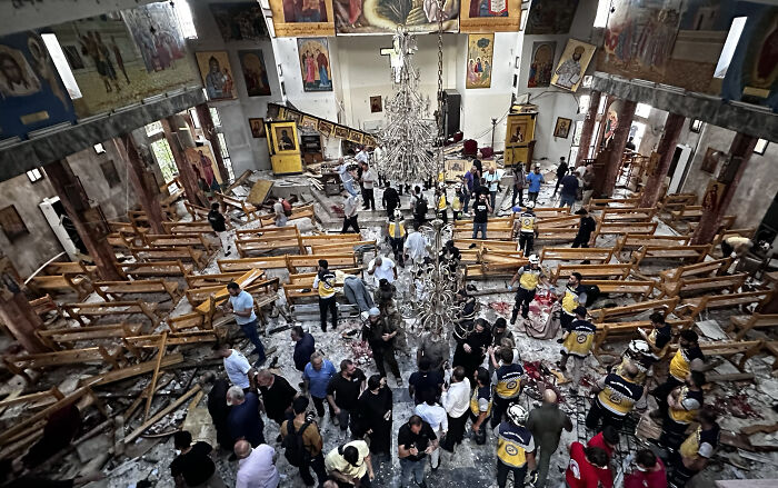 Greek Orthodox church in Syria damaged after suicide bombing, with rescue workers and people amidst debris inside the building.