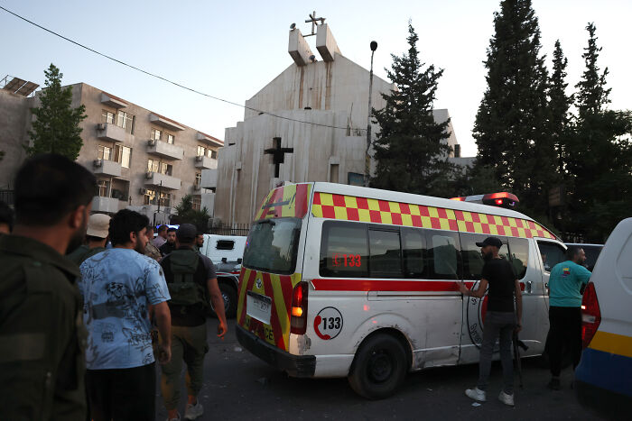 Ambulance and people outside Greek Orthodox church in Syria after suicide bombing causing multiple casualties.