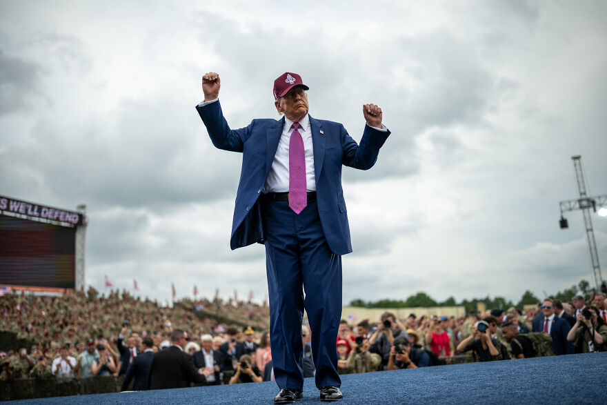 Man in navy suit and red hat at rally with crowd and photographers, related to Trump Organization gold phones news.