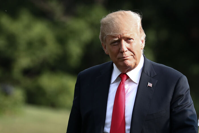 Donald Trump outdoors in a dark suit and red tie, linked to discussion of possible pardon for Ghislaine Maxwell.