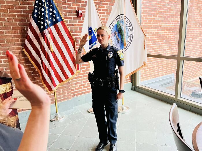 Off-duty cop in uniform taking oath near American flag in a bright room with brick walls and large windows.