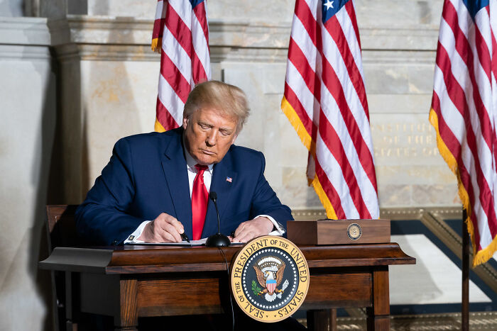 Former president at a desk with US flags, symbolizing Senate cuts to foreign aid and public broadcasting funding.
