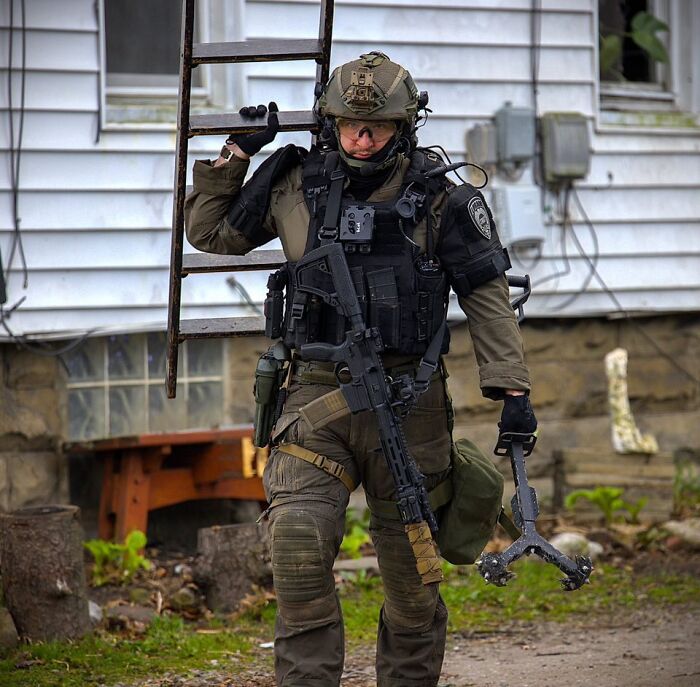 Ohio police officer in tactical gear carrying ladder and tool during operation related to ambush shooting investigation