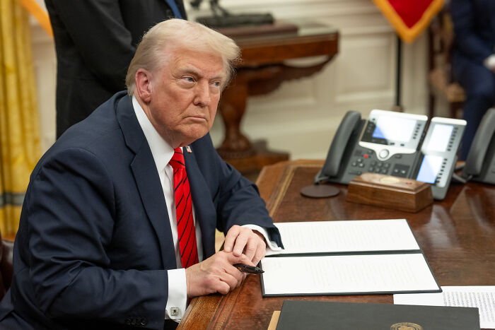 Former President Trump sitting at a desk with documents, highlighting Mark Ruffalo and Joe Rogan ICE raids debate.