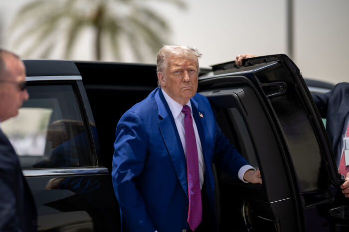 Donald Trump in a blue suit exiting a black vehicle, linked to discussions about Trump biographer and Elon Musk drug use claims.