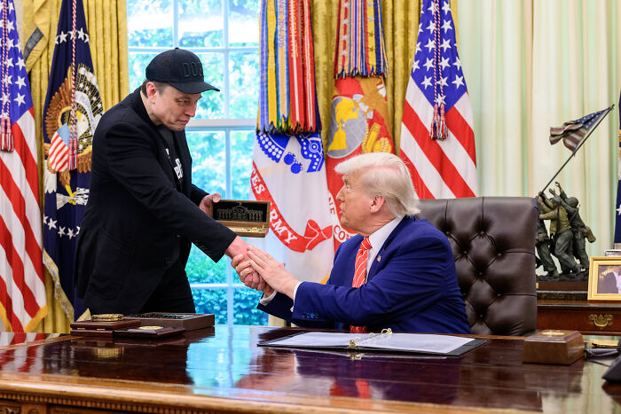 Elon Musk shaking hands with Donald Trump in the Oval Office amid discussion of Trump biographer claims.