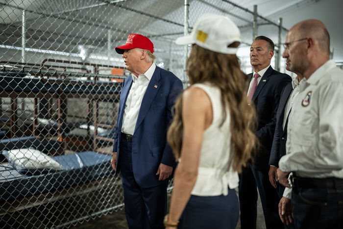 Donald Trump wearing red hat and navy suit inside detention facility with officials, related to Hannibal and ICE flight story.