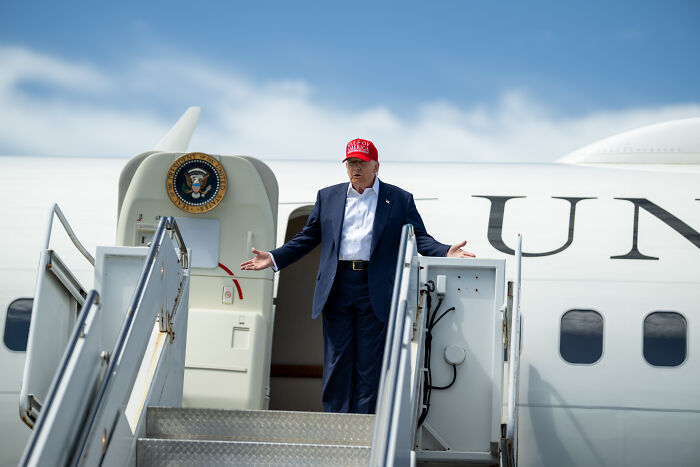 Former President Trump in red hat standing at Air Force One stairs, related to asylum and U.S.-Mexico border policies.