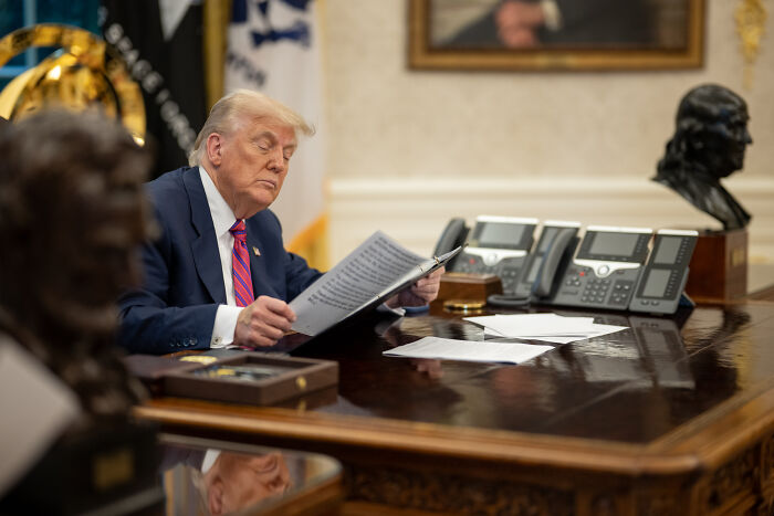 Former president reading documents at a desk with busts, relating to U.S. Olympic Committee transgender athletes ban.