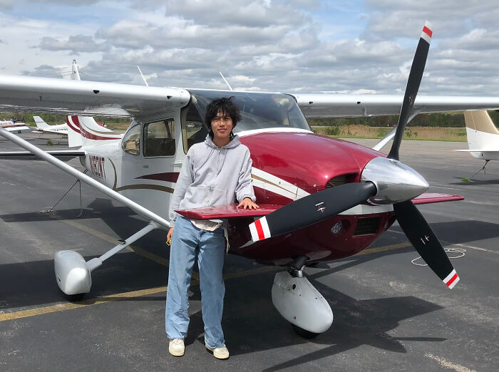 US teen standing beside small red and white airplane on runway during solo flight to support cancer cause.