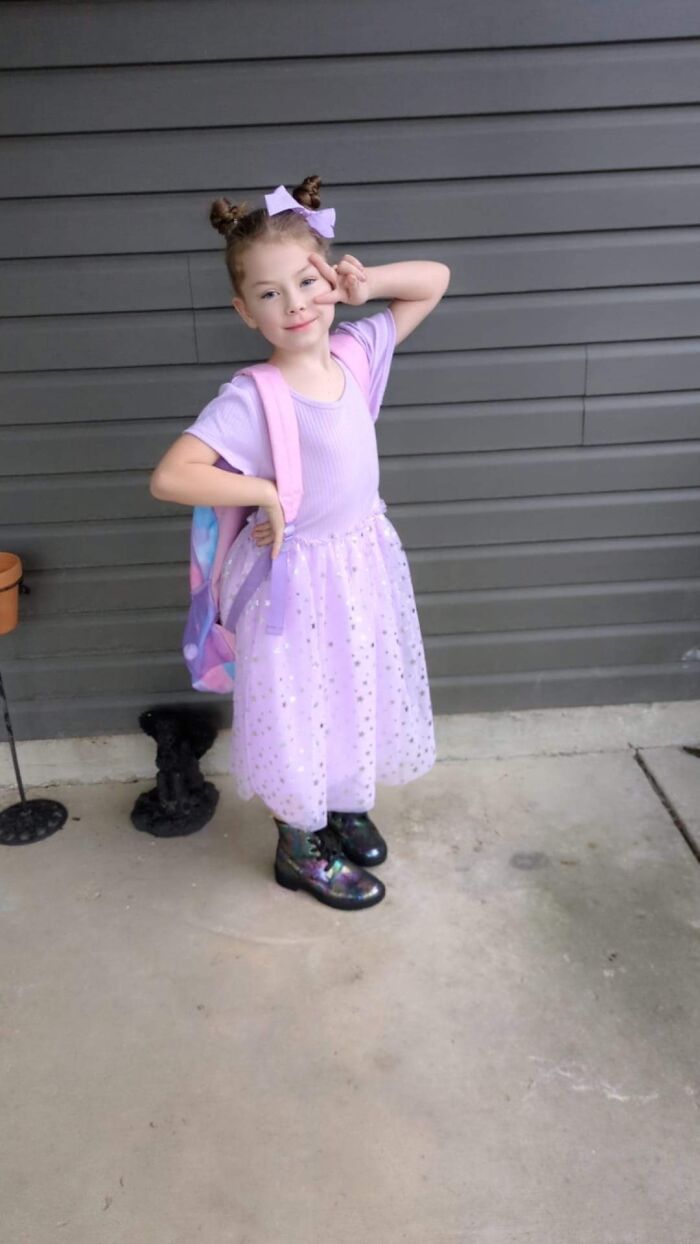 Young girl wearing a purple dress and backpack, posing with peace sign, main SEO keyword girl drowning in crowded pool during lesson